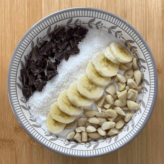 un bol healthy parfait après une bonne séance de sport. Il est composé de yaourt, de chocolat, d'une banane, de noix de coco râpée et d'amandes effilées