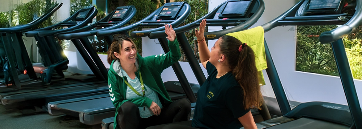 Deux femmes dans une salle de sport Elancia assises sur des tapis de course en train de se taper dans la main - Offre parrainage Elancia